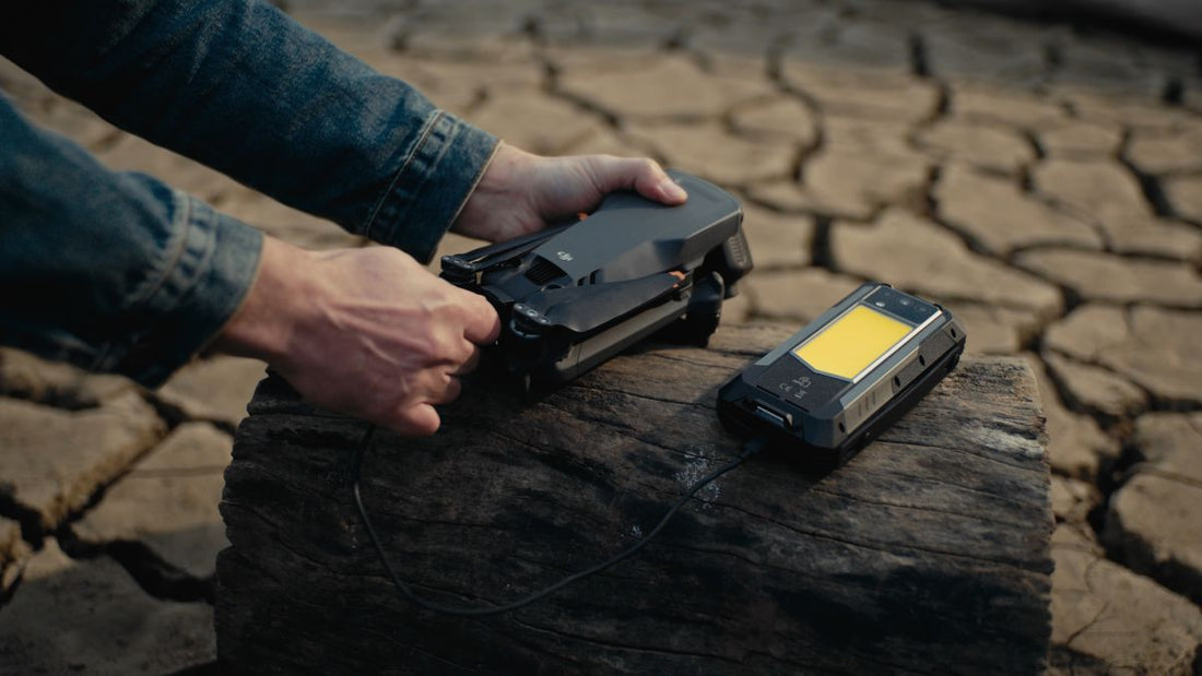 Person handling two rugged smartphones on a tree stump surrounded by dry, cracked ground.