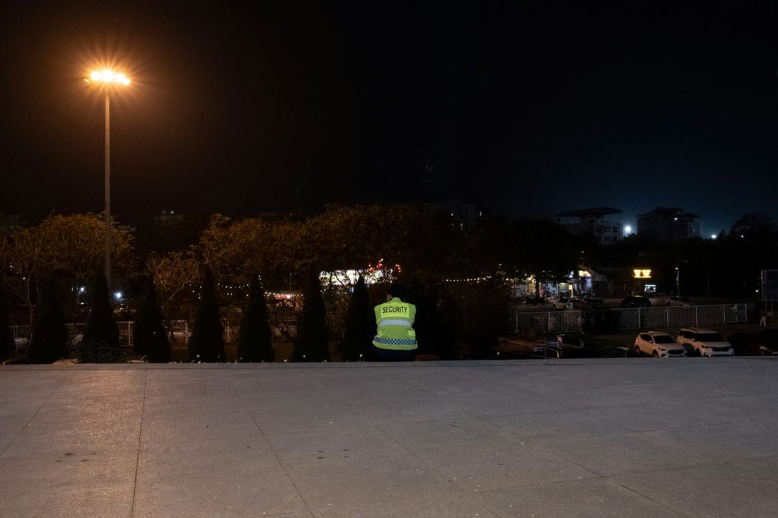 Security guard in a reflective vest standing alone in a dimly lit parking area at night.
