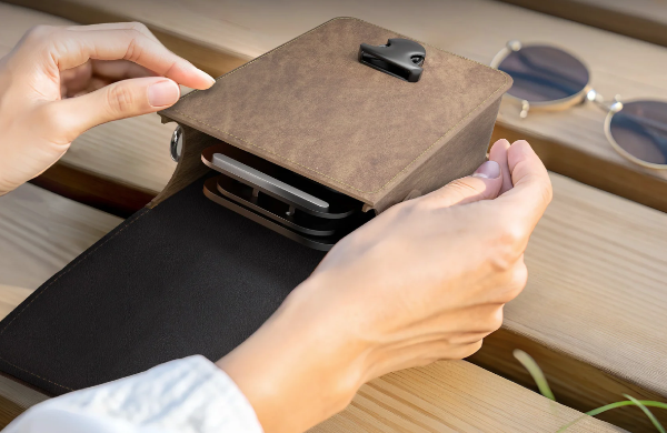 Person opening a brown leather phone pouch while seated indoors