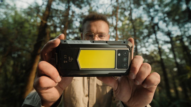 Person holding a yellow Oukitel WP100 Titan rugged phone in a forest
