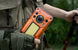 Person holding an orange Oukitel WP500 Ultra rugged phone in a natural setting